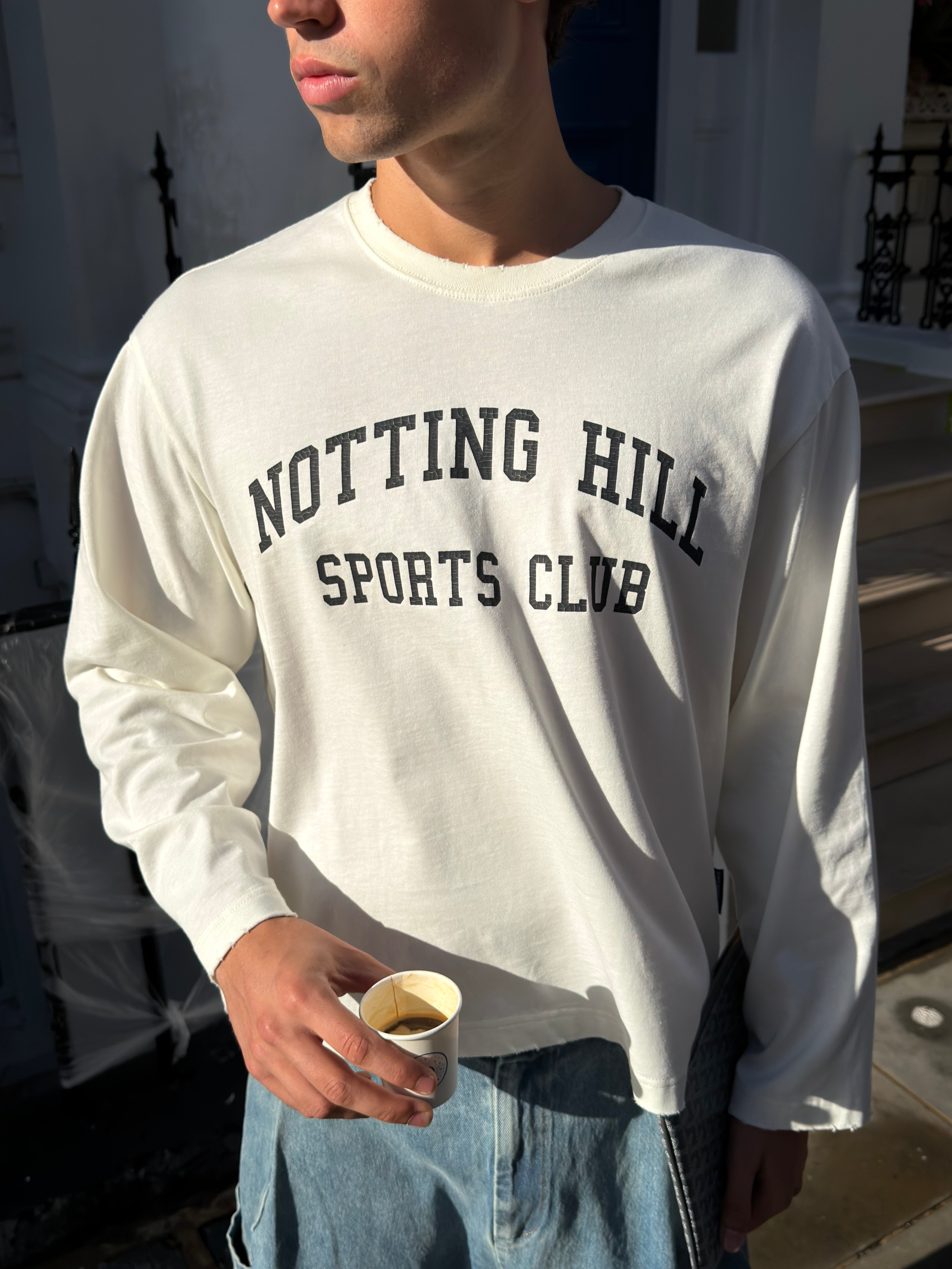 White Notting Hill Sports Club long-sleeve tee, front view, waist-up, worn by a model outdoors