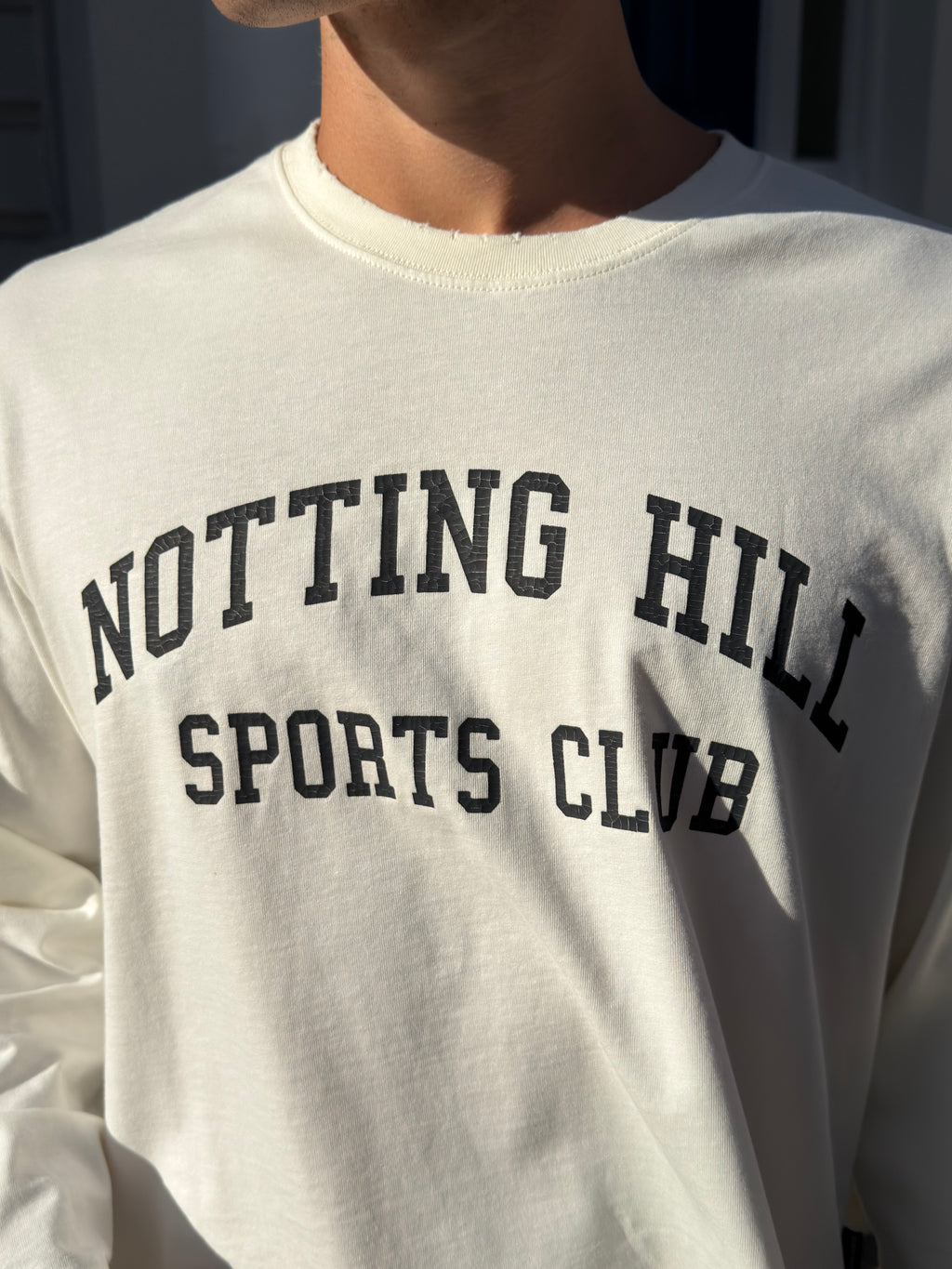 White Notting Hill Sports Club long-sleeve tee, close-up of the arched print and distressed collar