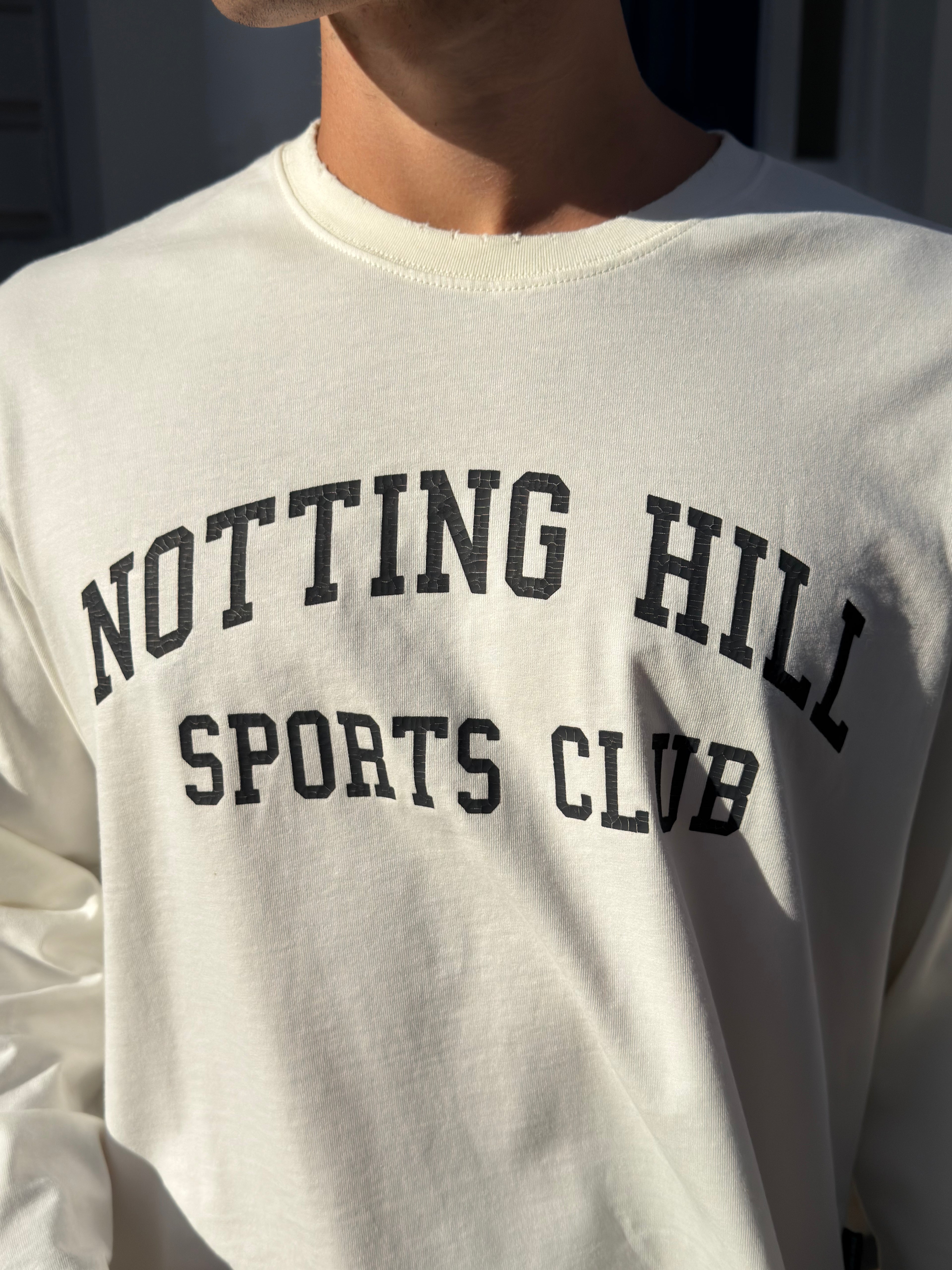 White Notting Hill Sports Club long-sleeve tee, close-up of the arched print and distressed collar