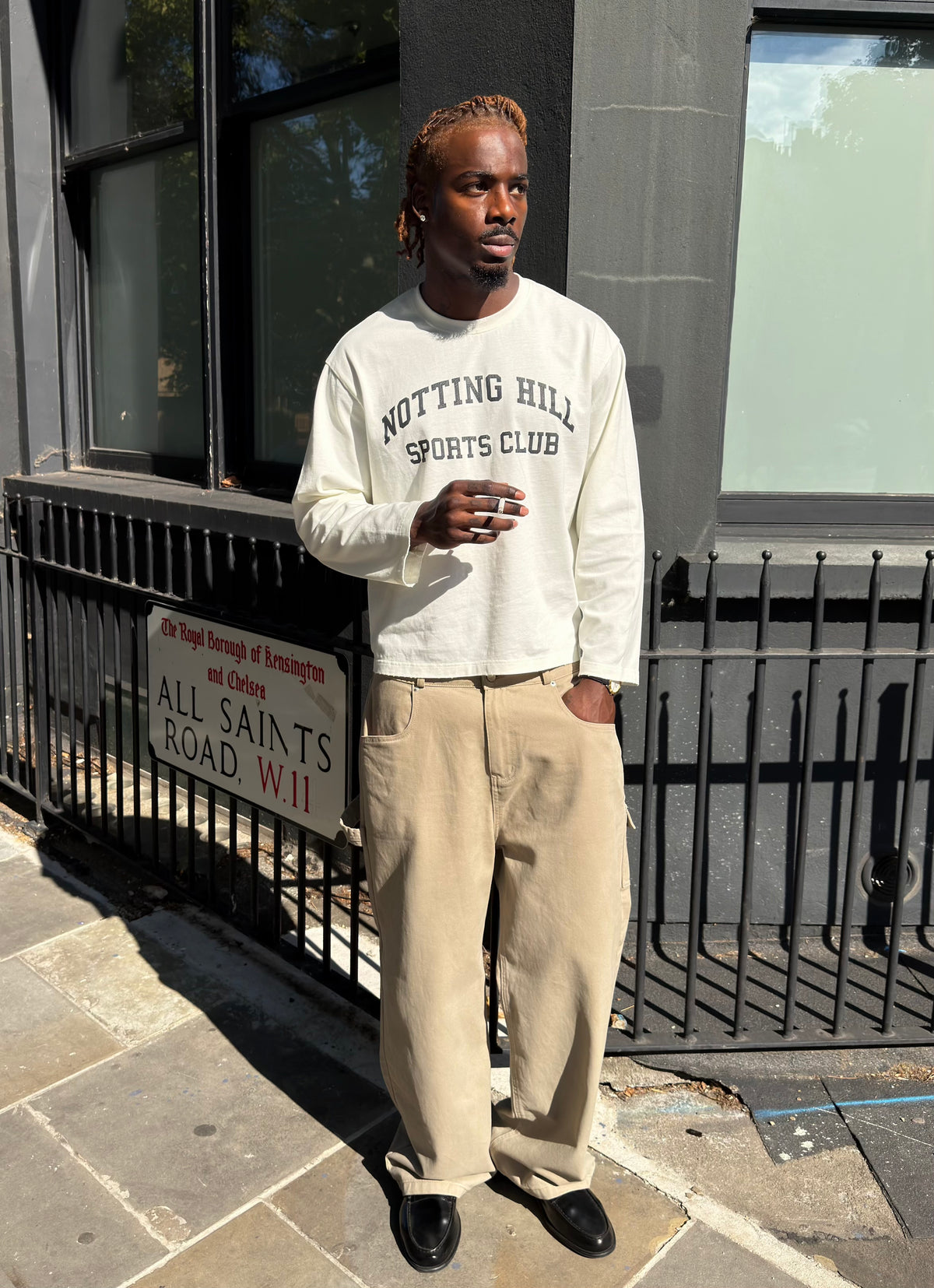 White Notting Hill Sports Club long-sleeve tee, full-length, worn by a model by a street sign