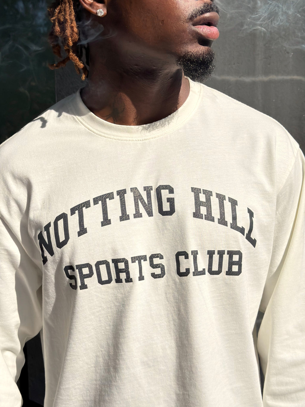 White Notting Hill Sports Club long-sleeve tee, close-up of the print, worn by a model looking away